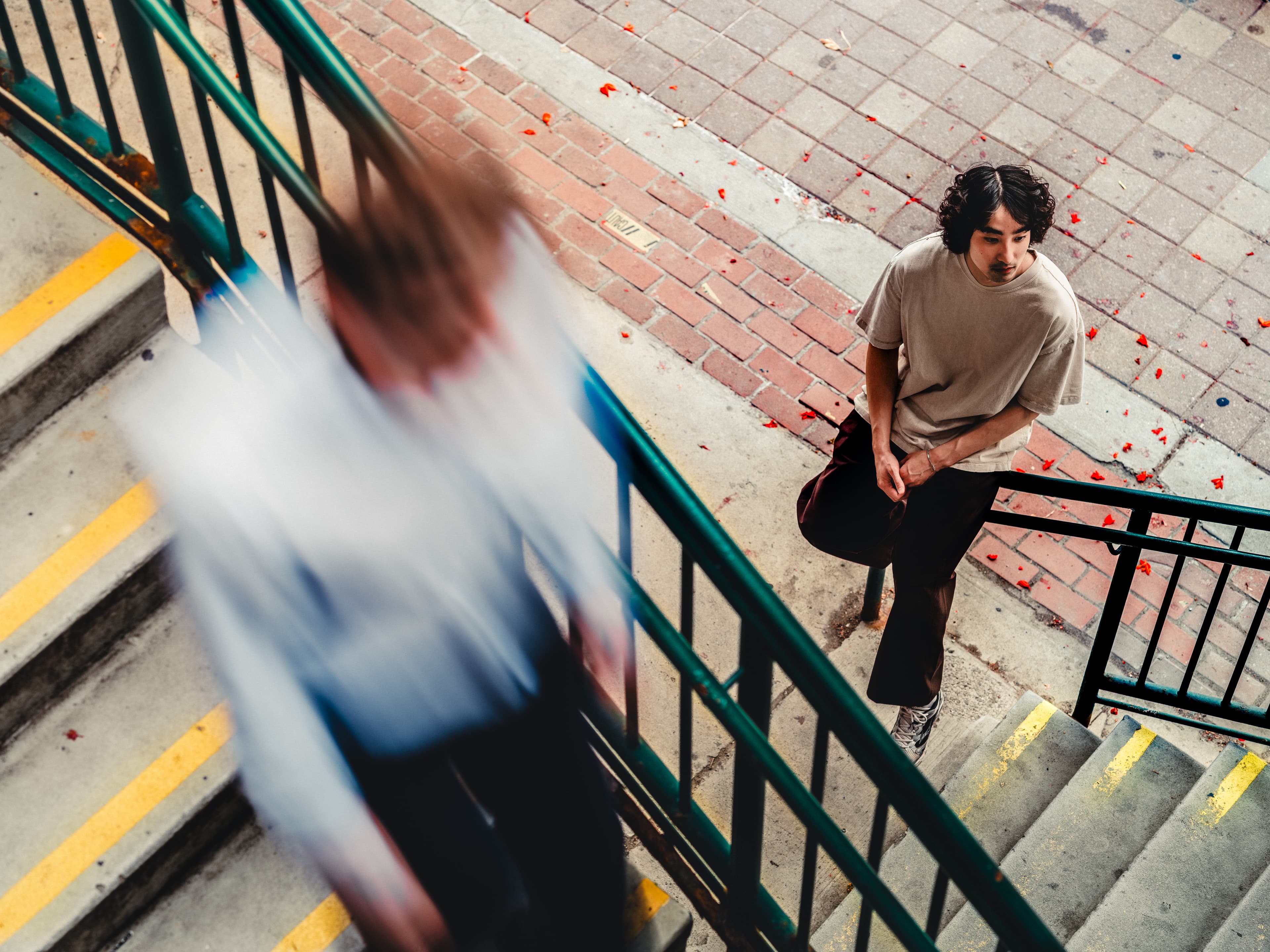 Overhead shot looking down at a man sitting on the railing at the bottom of a flight of stairs
