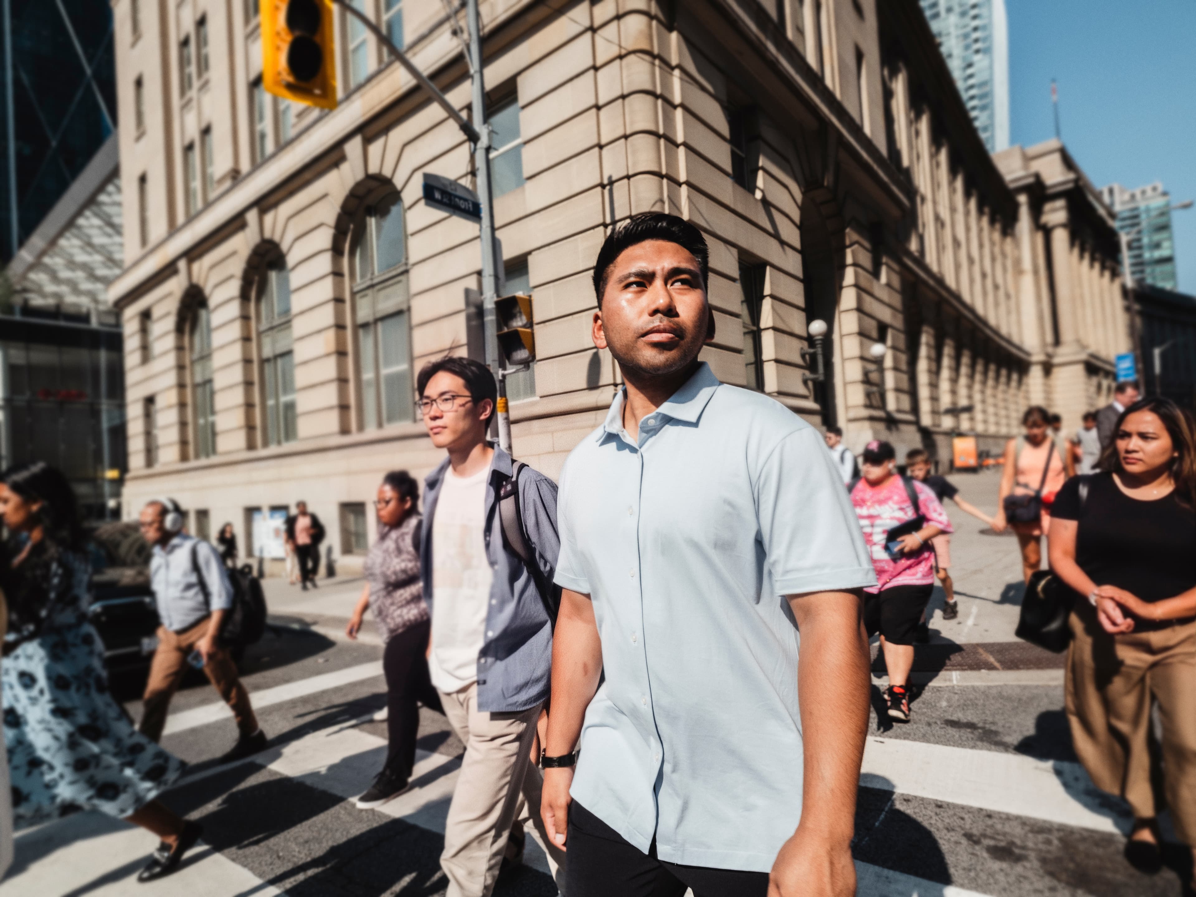 Close wide shot of a man in a button-down shirt crossing a busy city crosswalk