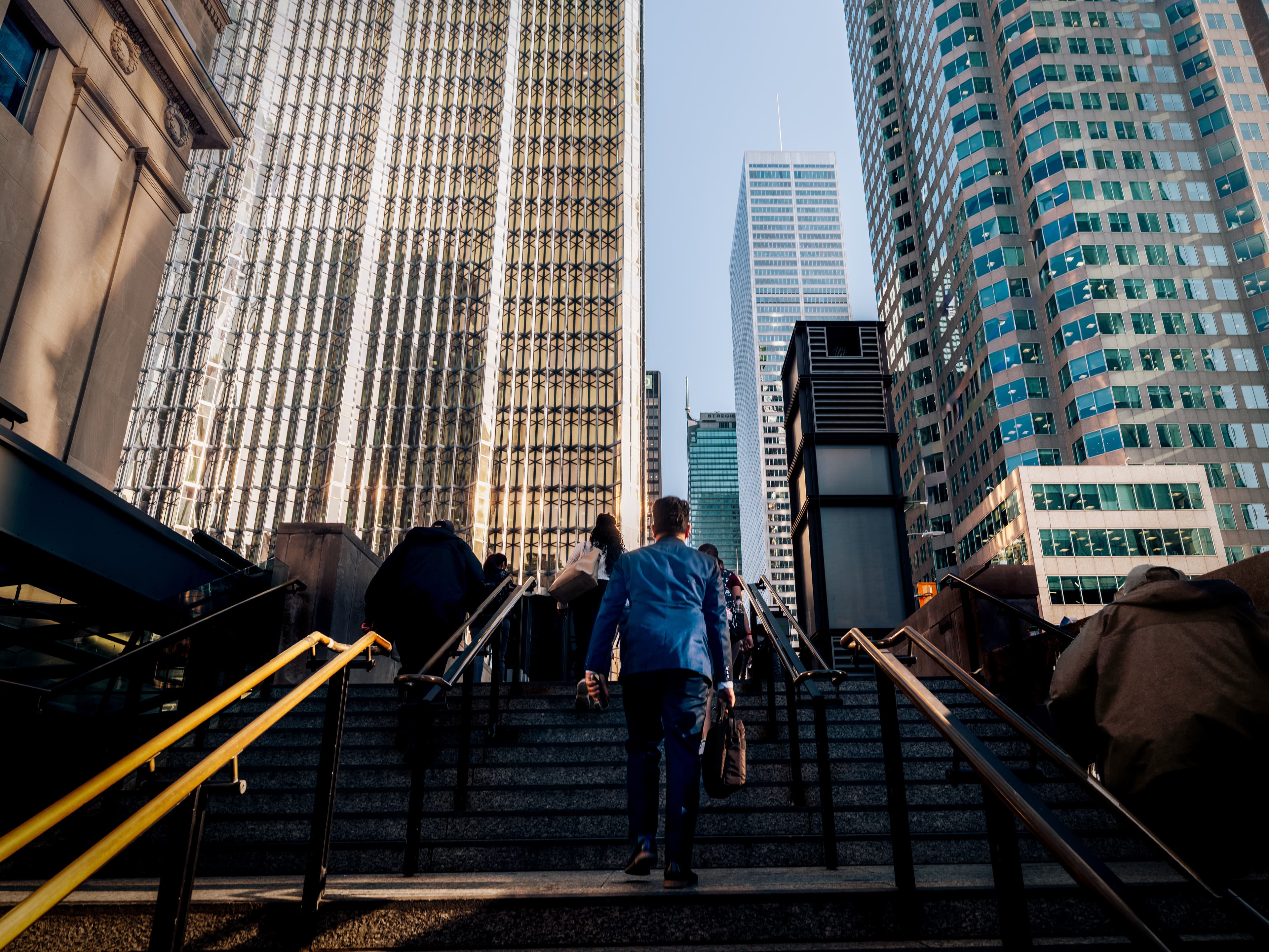 Man in suit walking up a flight of stairs up to downtown office buildings